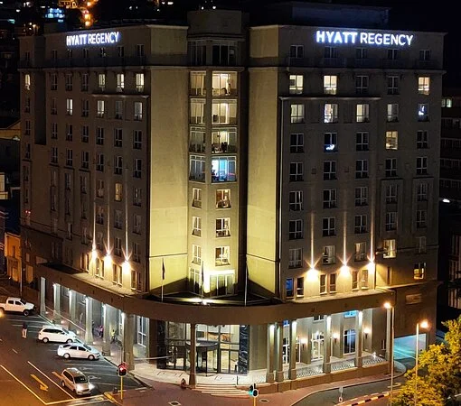 The Hyatt Regency Cape Town at night, its name lit on both corners of the building